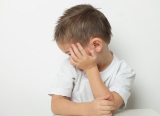 Small boy hides the side of his face with one hand.