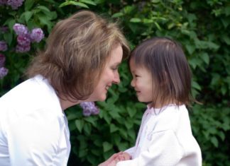 A woman and a girl face one another and smile.